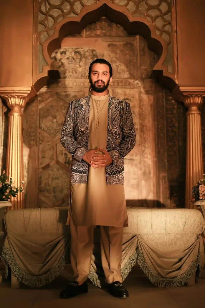 A man wearing ghazal beige tunic and trousers with an ornate dark gray paisley embroidered jacket