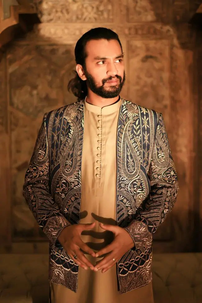 A man wearing a ghazal ornate dark blue and gold paisley embroidered jacket over a cream traditional tunic