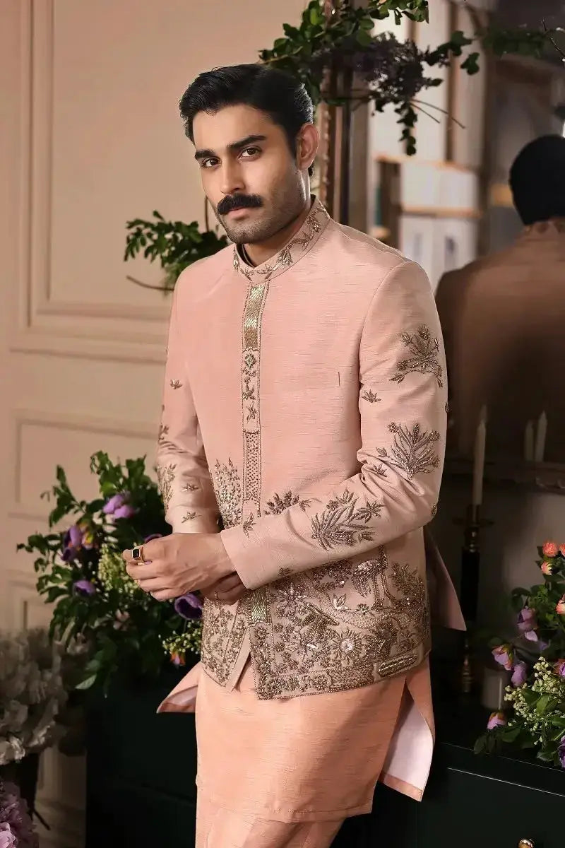 A man wearing a peach raw silk sherwani with gold embroidery and matching trousers in gulzar-e-raunaq design