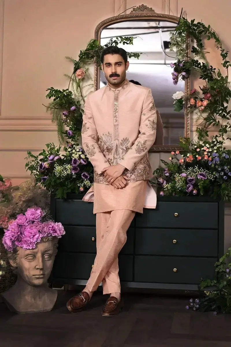 A man wearing a peach raw silk Gulzar-e-Raunaq suit with intricate gold threadwork on front and sleeves