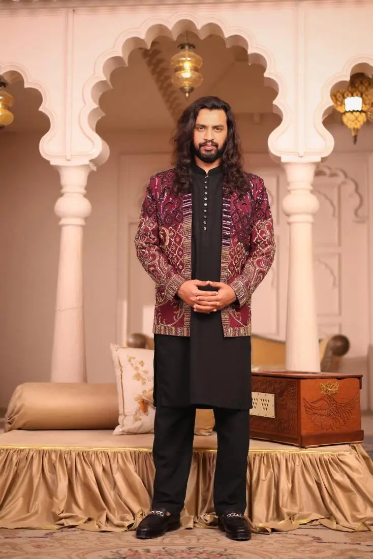 A man wearing a maroon and gold patterned embroidered Mirza jacket over black attire