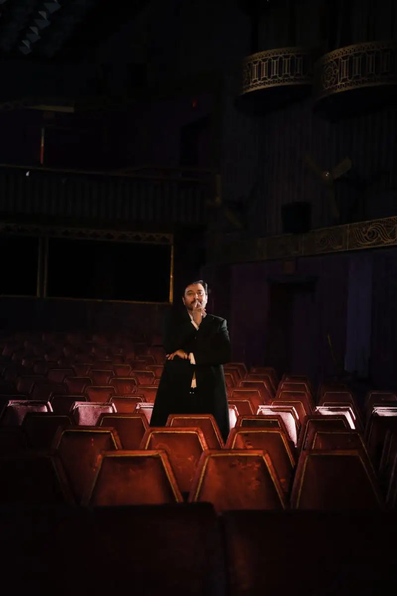 A solitary figure in a black coat stands illuminated by deep red theater seats in nadeem baig virsa-e-sitaaran edit26