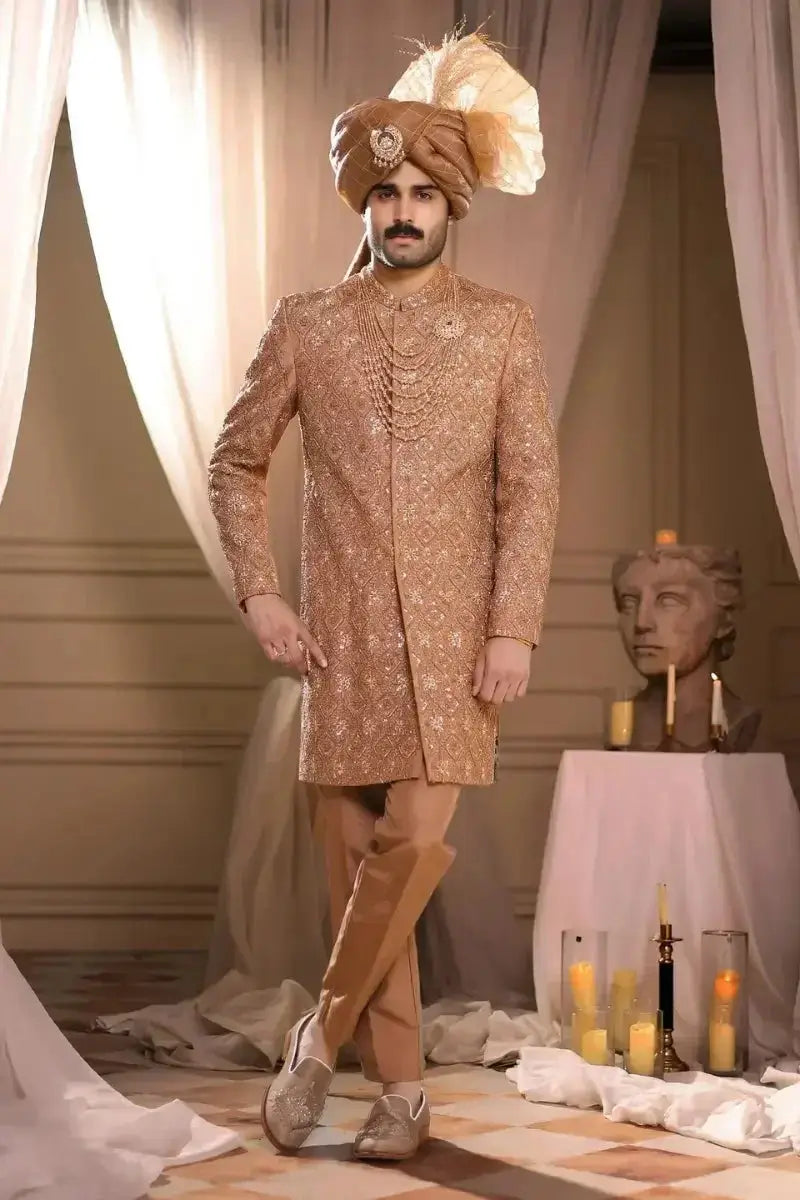 A man wearing a gold-embroidered pehlwani poshak with intricate floral patterns and matching trousers and footwear