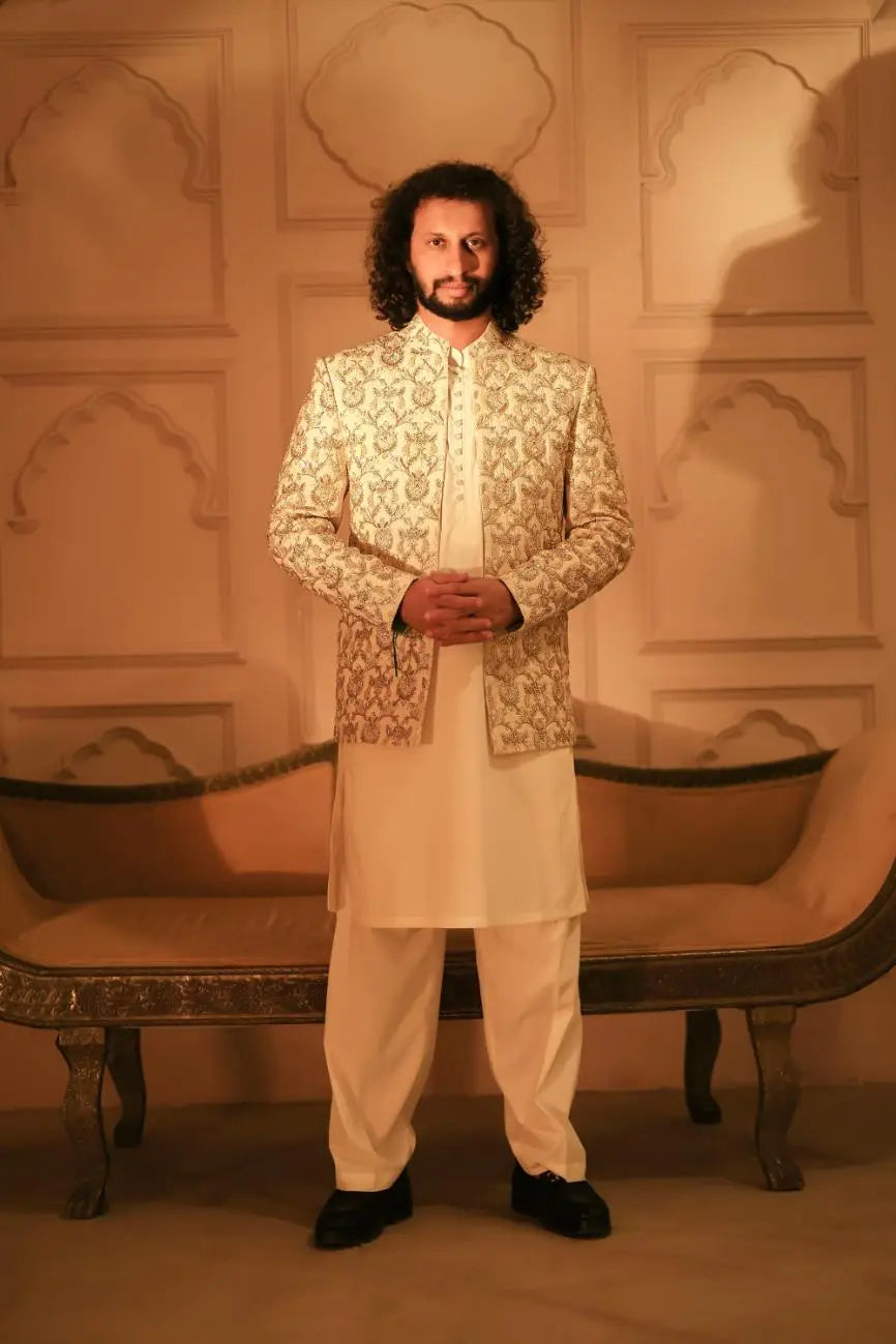 A man wearing the sultan cream jacket with intricate gold embroidery over a white kurta and trousers