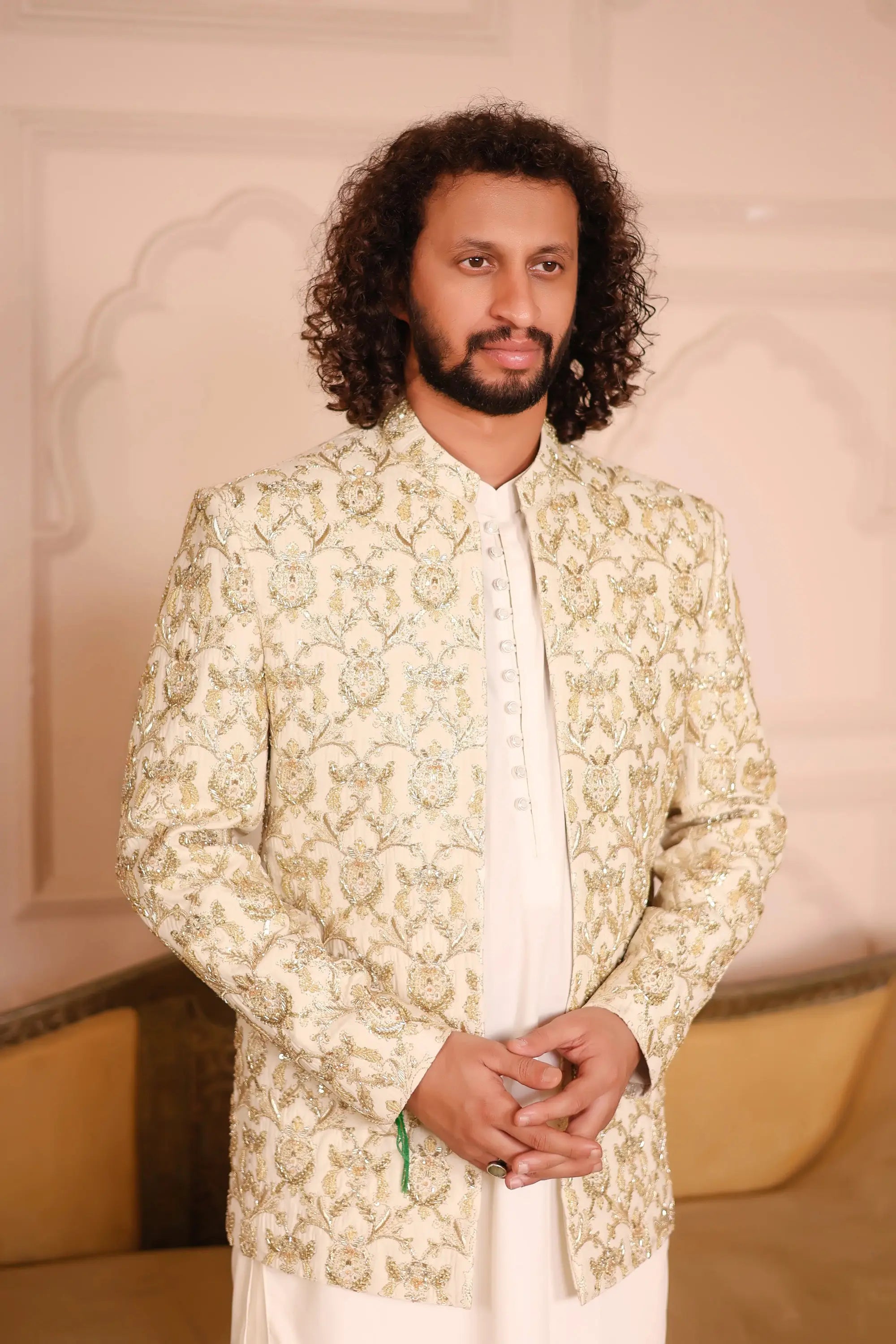 A man wearing a sultan cream-colored jacket with intricate green floral embroidery on the front