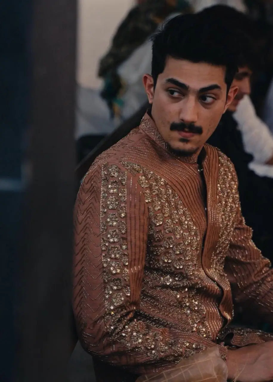 A man wearing a bronze-colored zarposh traditional jacket with intricate gold sequin and bead embroidery
