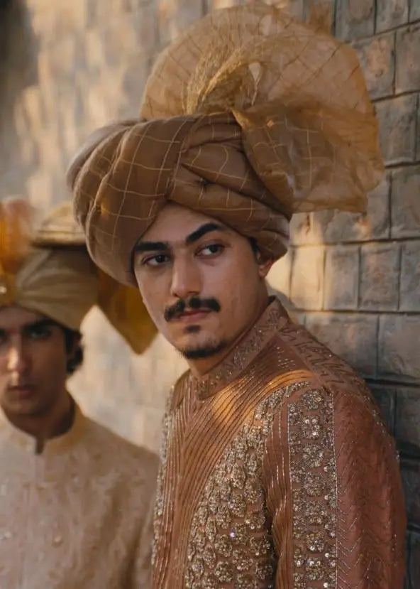 A man wearing a zarposh ornate gold-toned turban with checkered pattern and sheer fabric accents