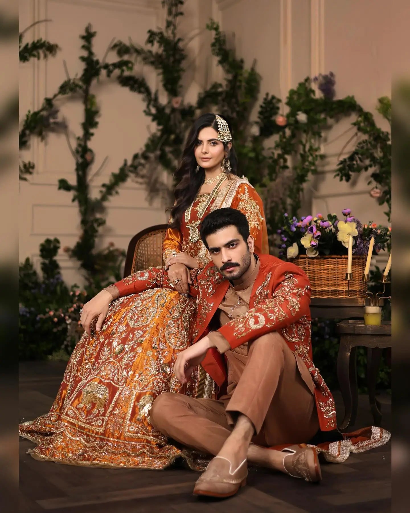 The woman wears a breathtaking lehnga choli in vibrant amber rust with ornate gold paisley embroidery from Ambar