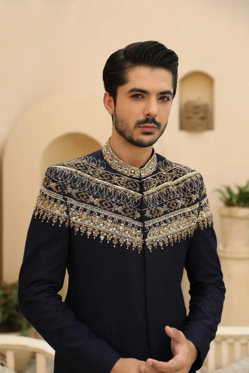 Azraq prince coat from raqeeb se collection in navy blue sherwani with intricate gold and silver embroidery along collar and shoulders