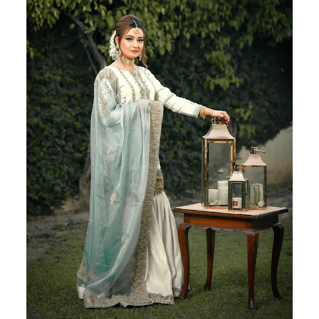 A woman in an ethereal light blue and white embroidered festive wardrobe holds three ornate lanterns beside a table