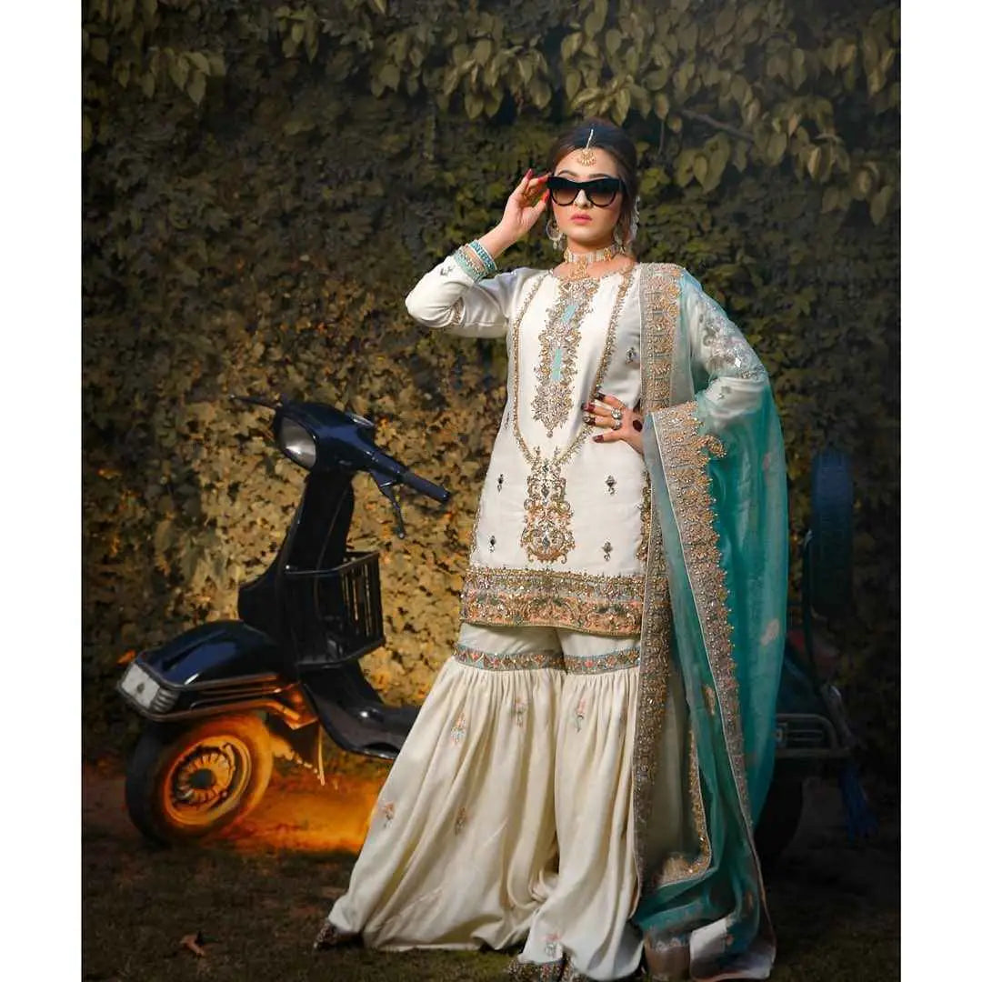 A woman wearing an ethereal meticulously crafted three-piece off-white and teal embroidered outfit with gold detailing