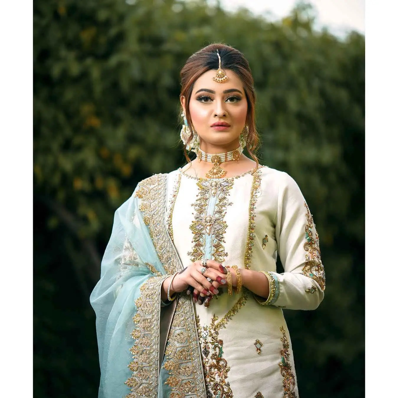 A woman wearing ethereal meticulously crafted three-piece off-white embroidered salwar kameez with gold thread detailing and light blue sheer dupatta for festive wardrobe