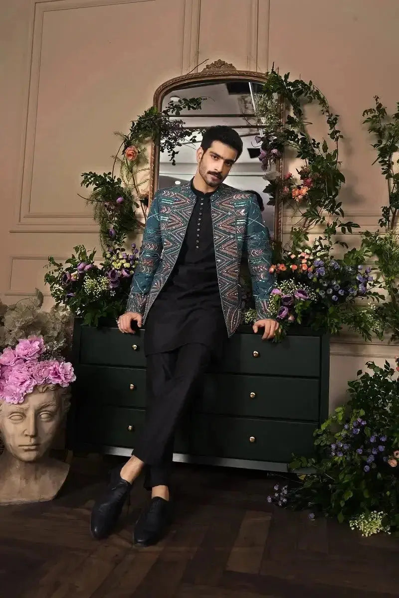 A man wearing a fakhar-e-jahan teal and gold embroidered blazer over black formal attire