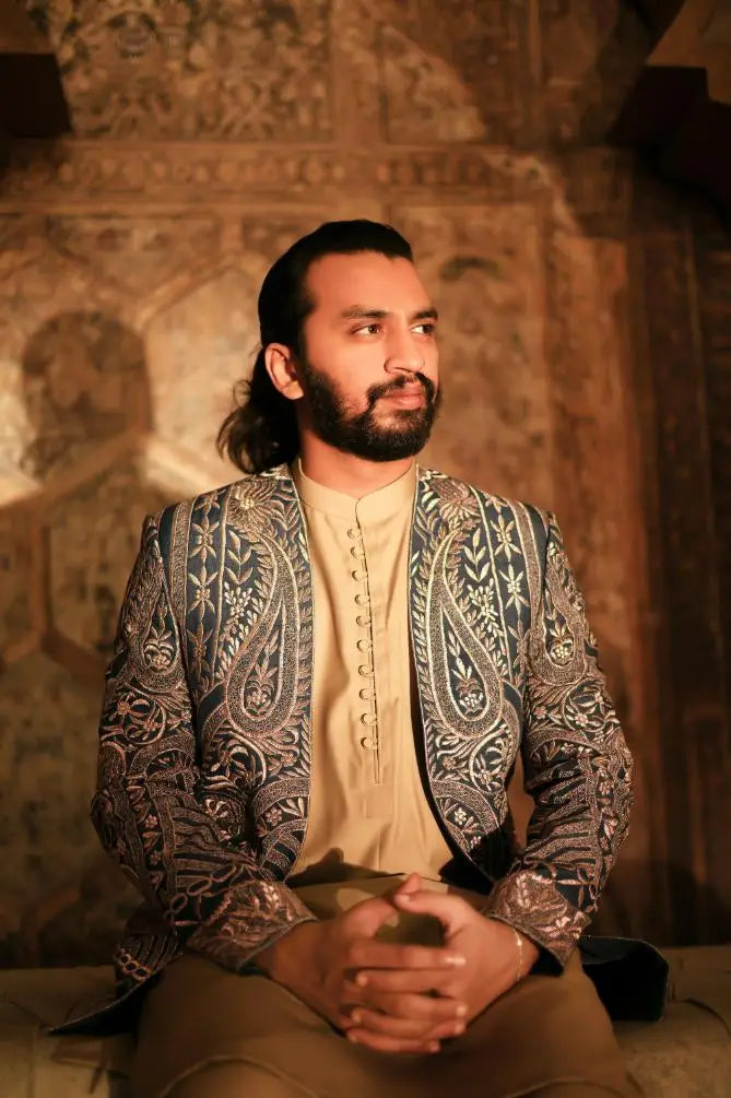 A man wears a dark blue and silver paisley-patterned embroidered blazer over a cream button-up shirt called Ghazal