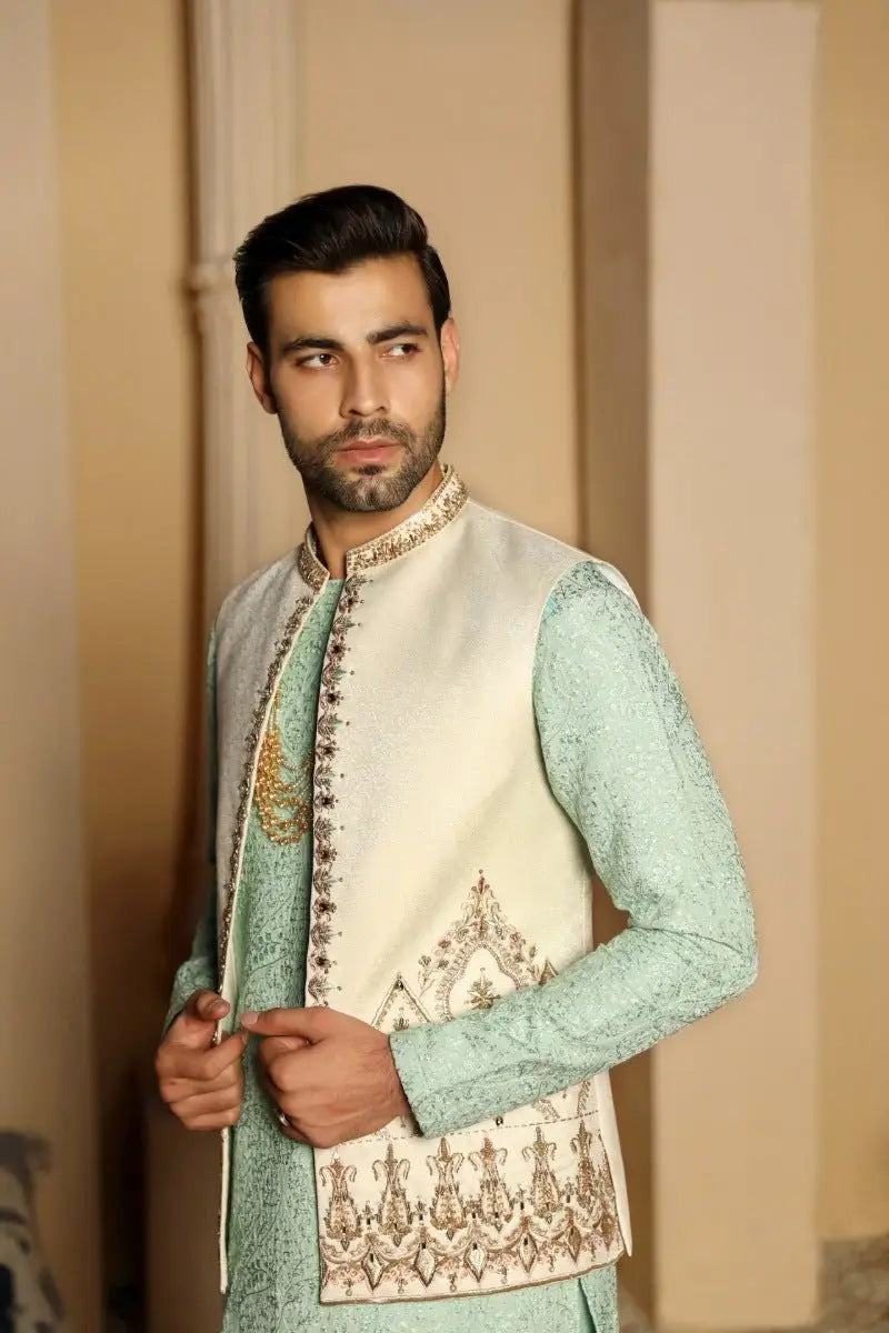 A man wearing a gulistan prince coat by ahsan tariq featuring a mint green embroidered vest with gold thread detailing