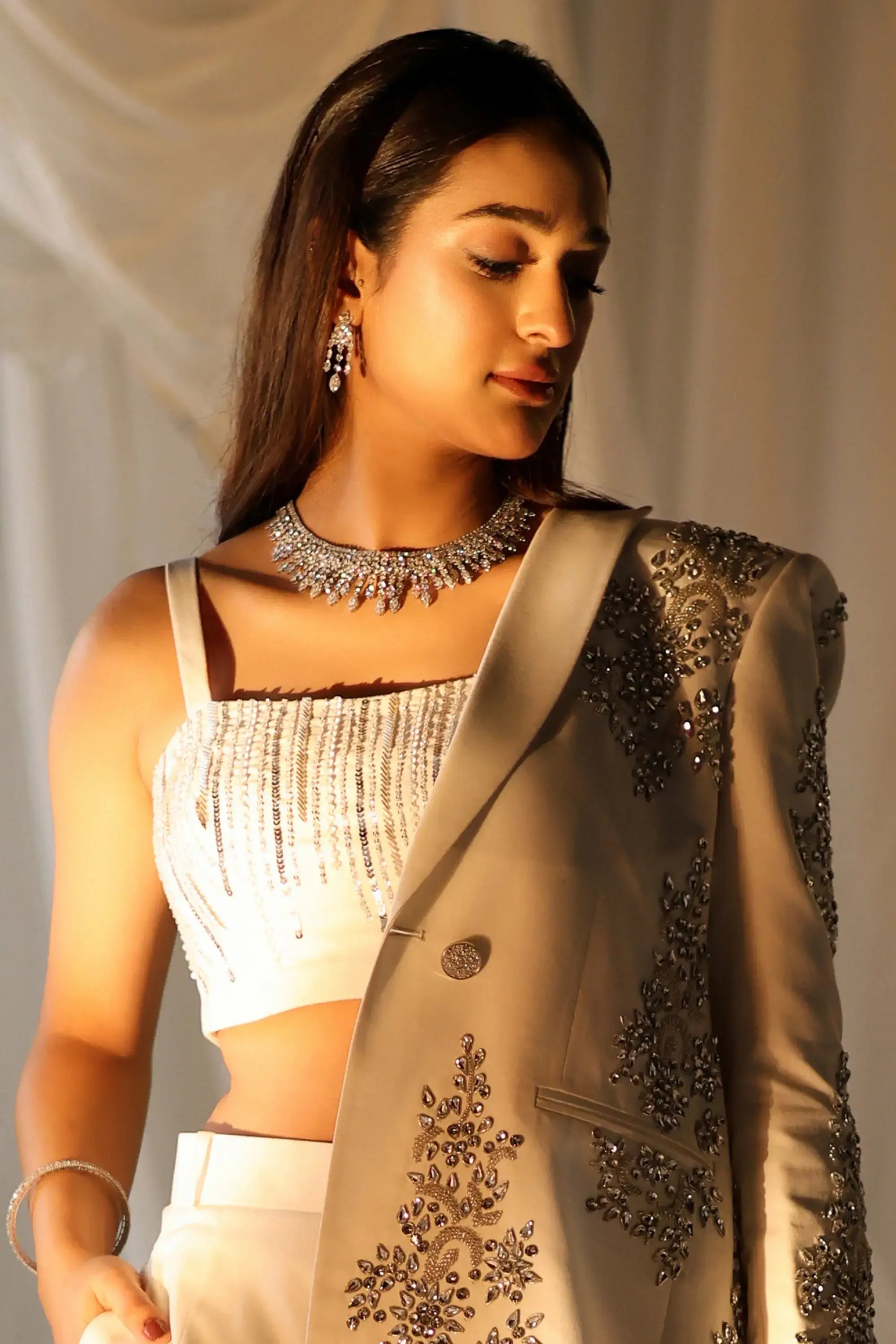 A woman wears ivory radiance formal wear by ahsan tariq featuring a beige blazer with gold and silver embroidery and a white sequined crop top