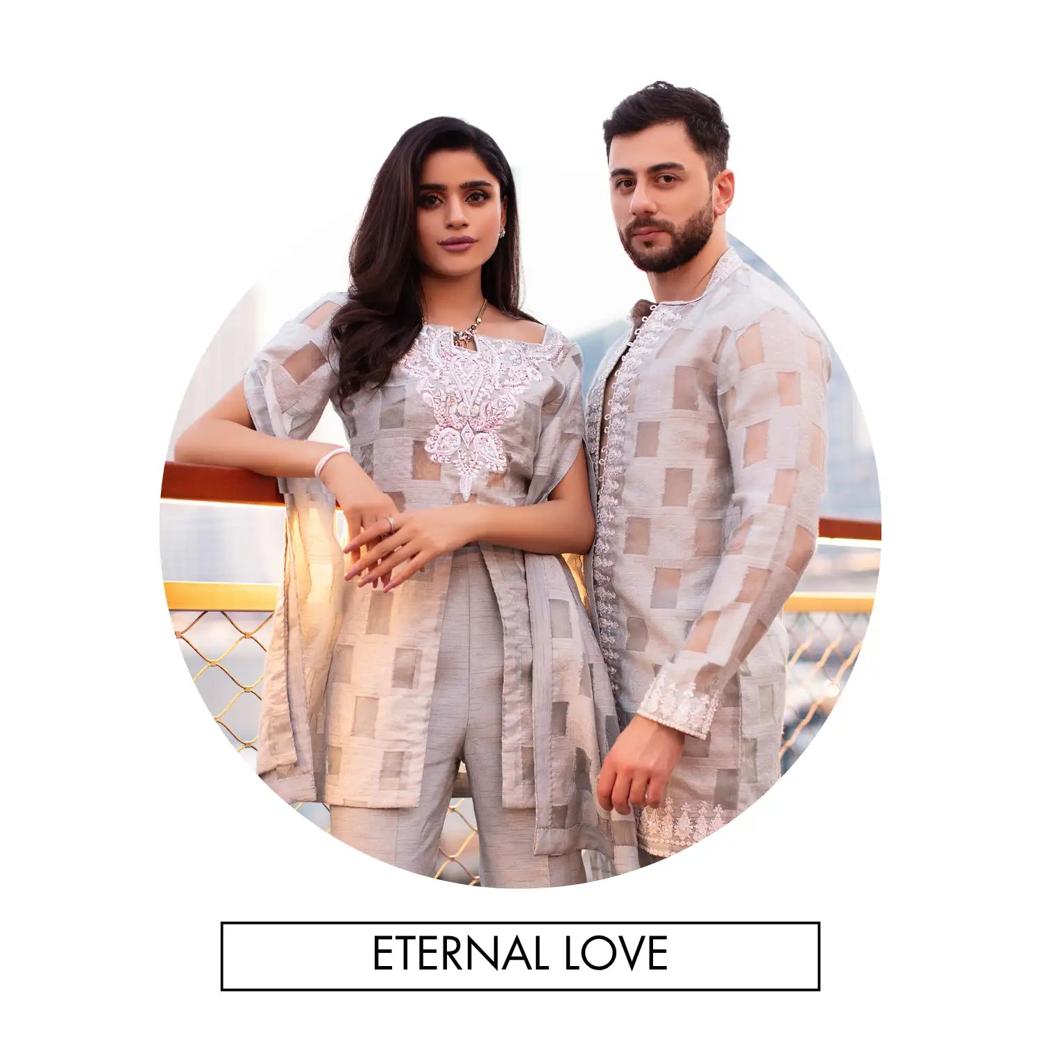 A matching light gray and beige patterned traditional outfit set for a couple, featuring intricate white embroidery on the woman’s top.