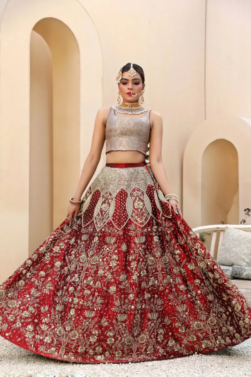 A woman wears malika lehenga with a red skirt featuring antique gold tilla embroidery and a silver-toned crop top by ahsan tariq