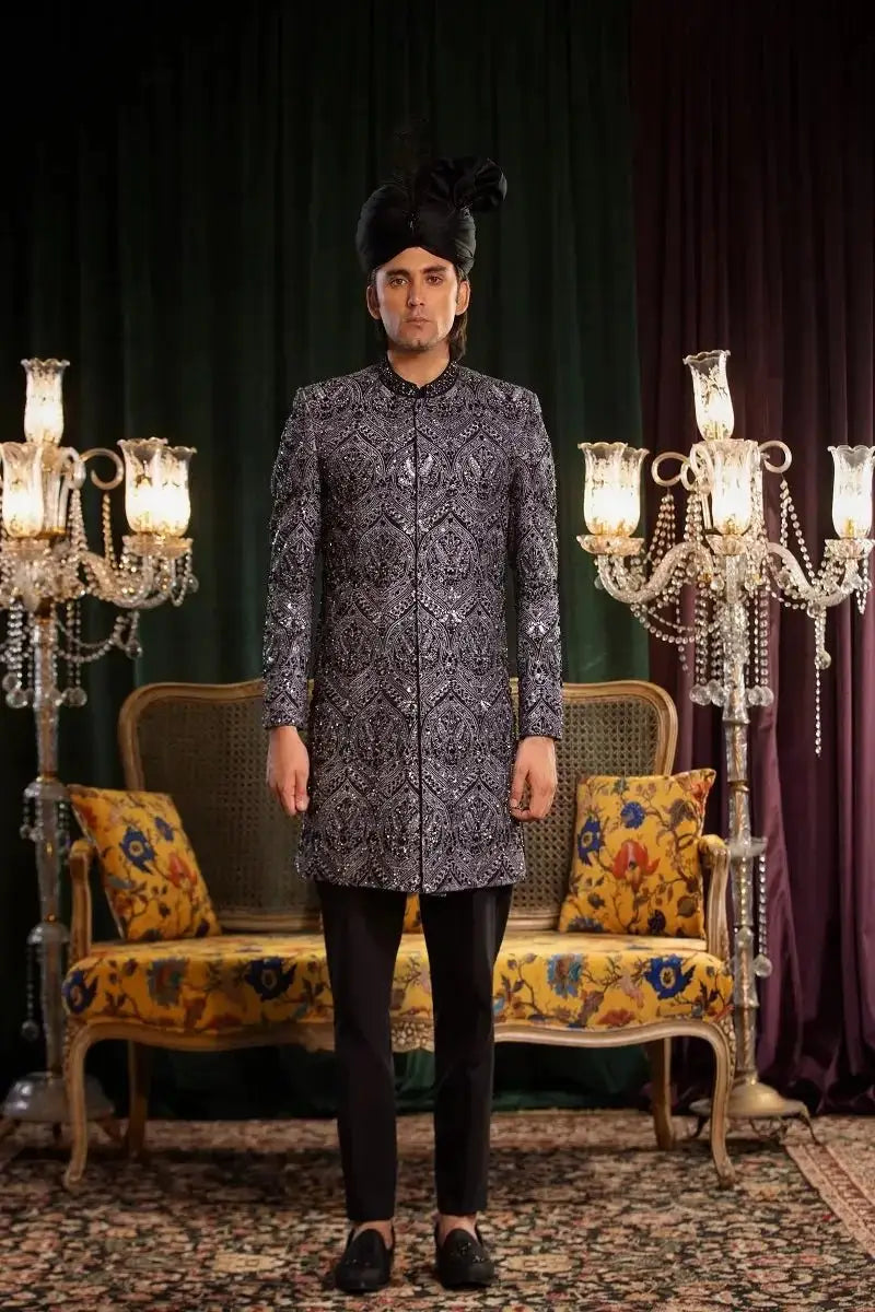 A man wearing a dark gray and black raw silk sherwani mastaan with intricate embroidery paired with black trousers