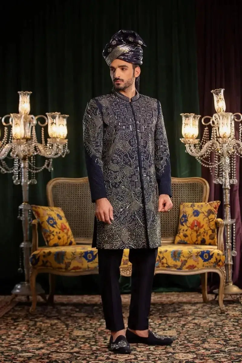 A man wearing a dark navy raw silk sherwani with silver paisley embroidery and matching trousers in Mastaan