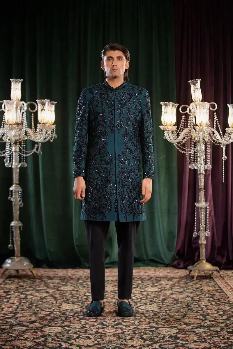 A man wearing mayameen dark teal sherwani with intricate silver threadwork and bead embroidery detailing