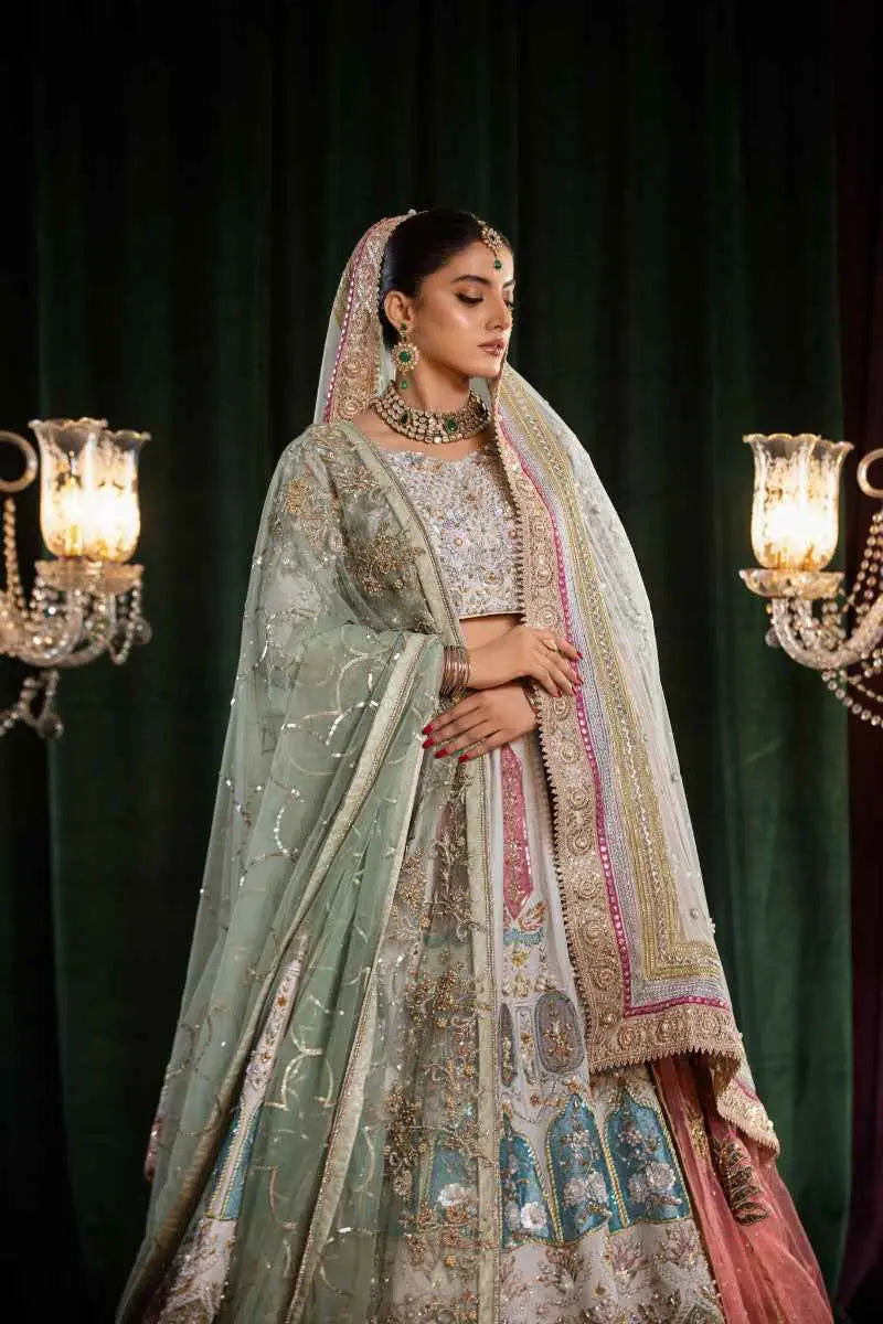 A woman wears the mehr-un-nisa ensemble featuring a light green and pink embroidered bridal lehenga with gold detailing