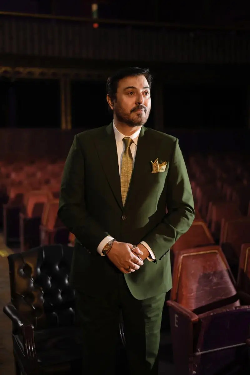 A man wearing a dark green tailored suit with a gold patterned tie and matching pocket square in nadeem baig virsa-e-sitaaran edit 26