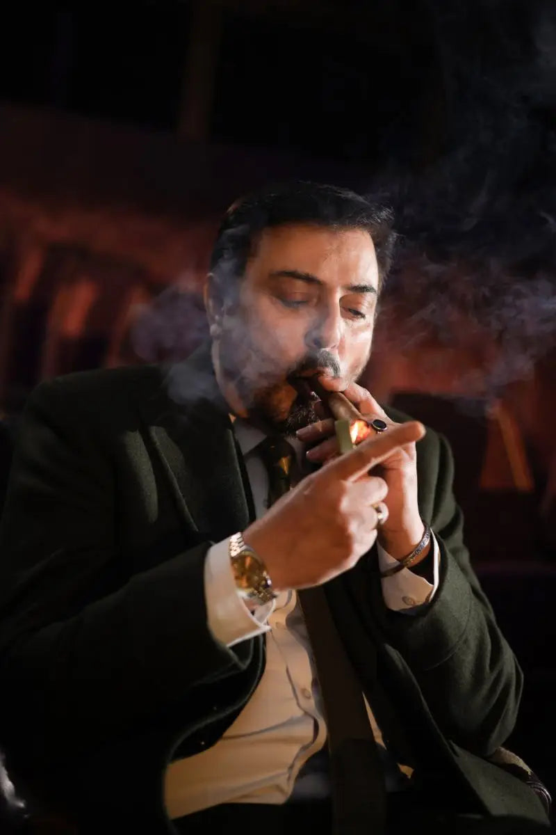 A man in a dark suit and white shirt smokes a cigar wearing a gold watch and bracelets in nadeem baig virsa-e-sitaaran edit26