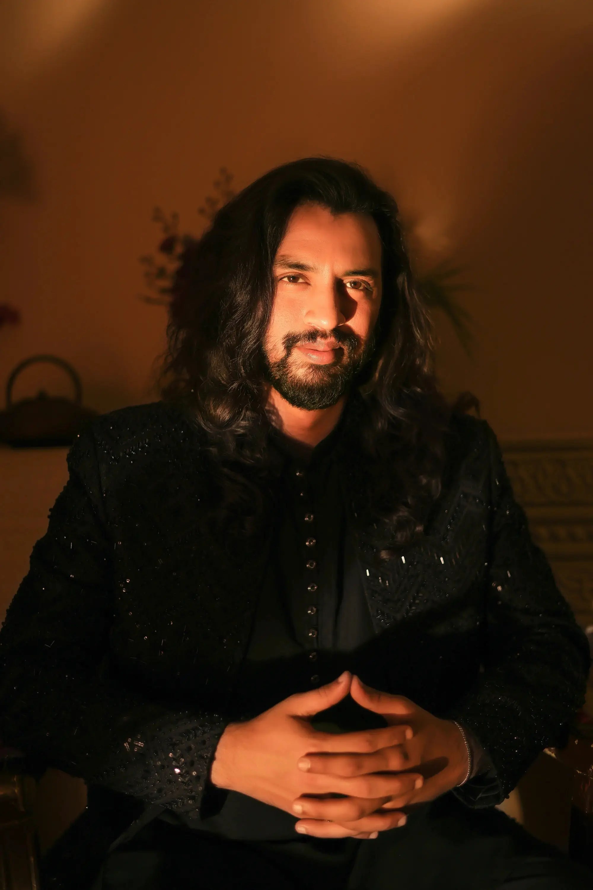A man wearing an elegant black sequined jacket with long dark hair and beard in the product nawab