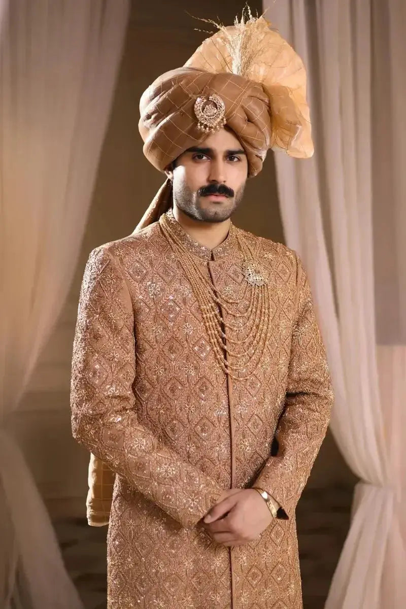A man wearing a gold-embroidered pehlwani poshak with diamond-patterned detailing and layered beaded necklaces