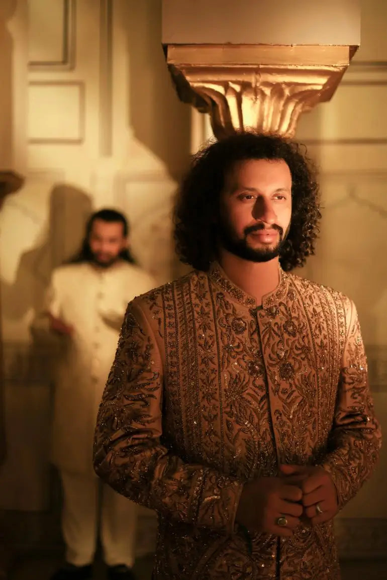 A man wears a qalandar sherwani with ornate gold embroidery and intricate patterns in shimmering fabric