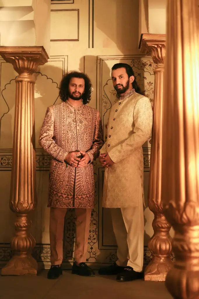 Two men wearing qalandar sherwani outfits one in detailed gold cream pattern and the other in solid light beige fabric