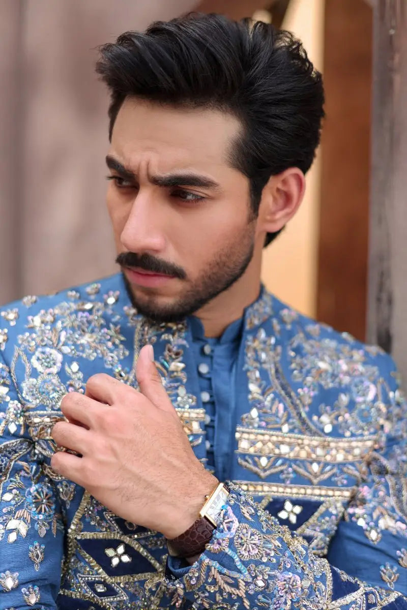 A man wearing a blue embroidered prince coat with gold and silver threadwork from ahsan tariqs ishq collection QALB