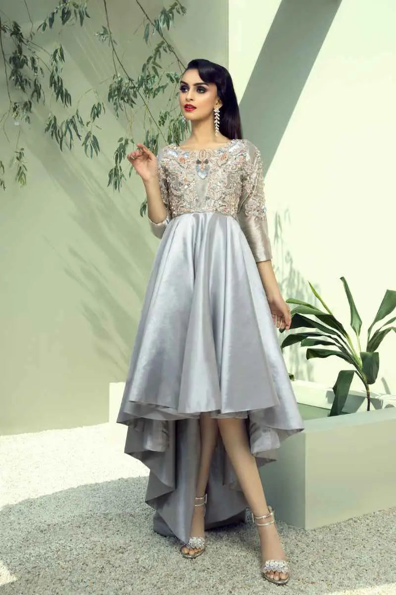 A woman wears a silver satin high-low gown with intricate lace and beaded embellishments in ahsan tariqs mesmerizing blend quicksilver