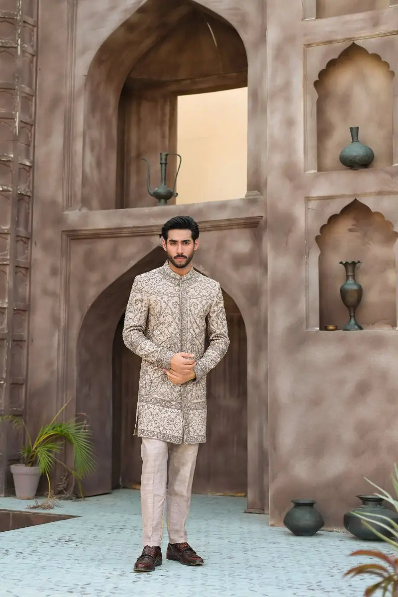 A man wearing a beige sandskin sherwani with gold embroidery and matching trousers from ahsan tariqs ishq collection qurb