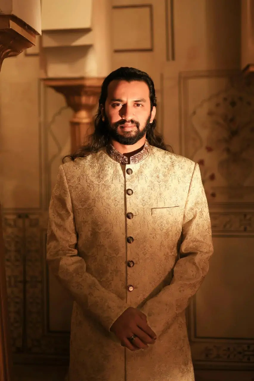 A man wearing a beige intricately embroidered sherwani with gold-toned buttons and detailed collar in ranjha design