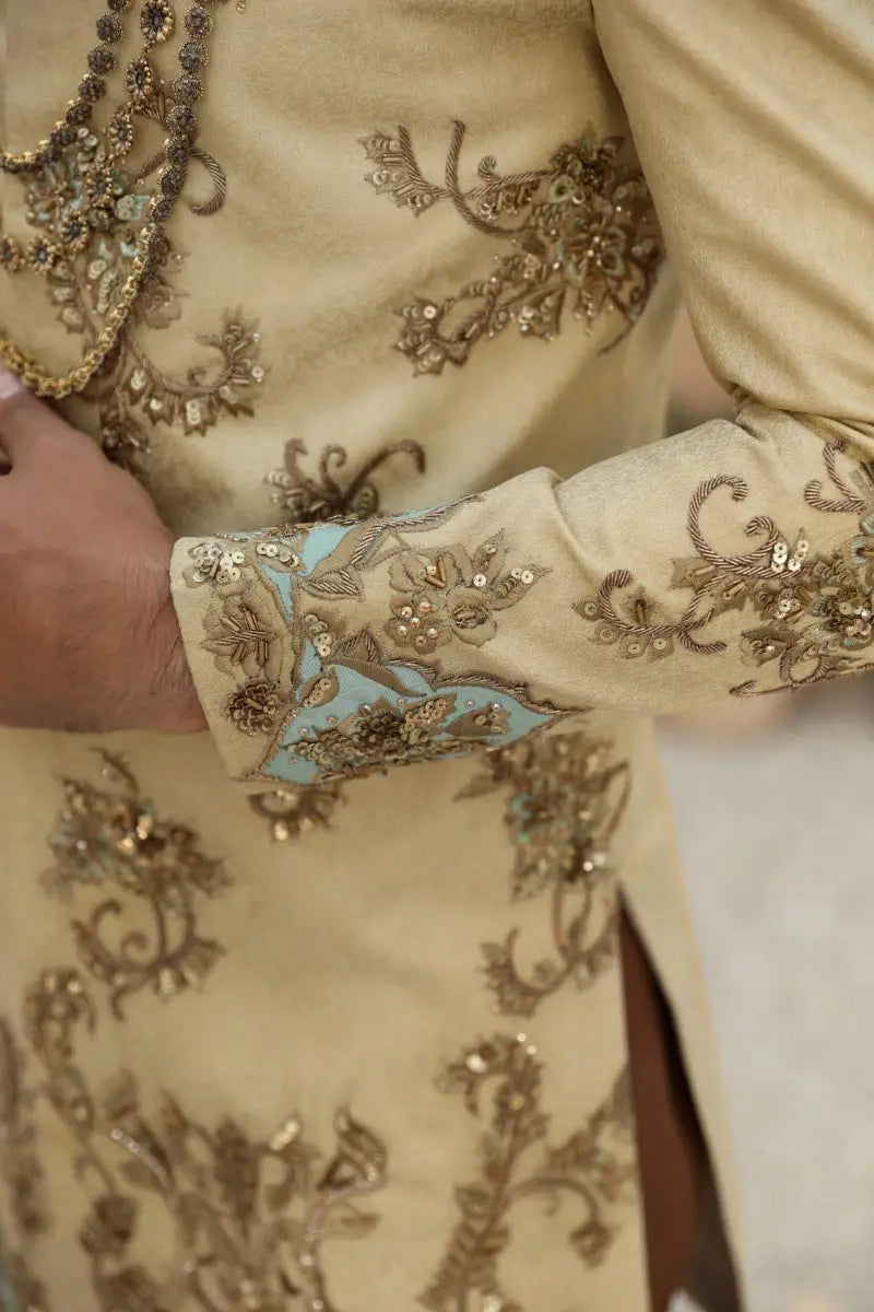 Cream-colored embroidered sherwani with gold thread and sequin detailing and light blue cuff panel from raqeeb se collection by ahsan tariq prince coat sahar