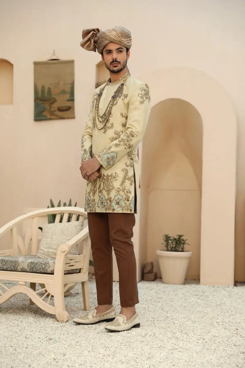 A man wearing sahar prince coat from raqeeb se collection in cream embroidered sherwani with antique gold and green details