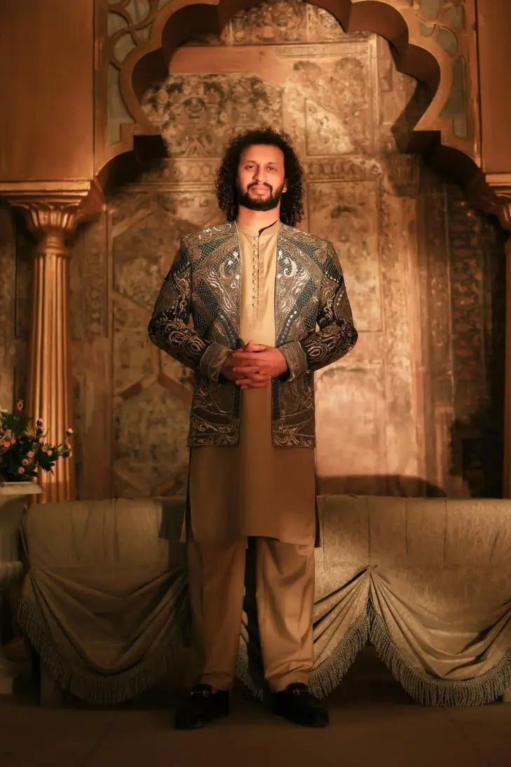 The man wears a shayar silver and navy blue embroidered jacket with intricate paisley patterns over a cream kurta