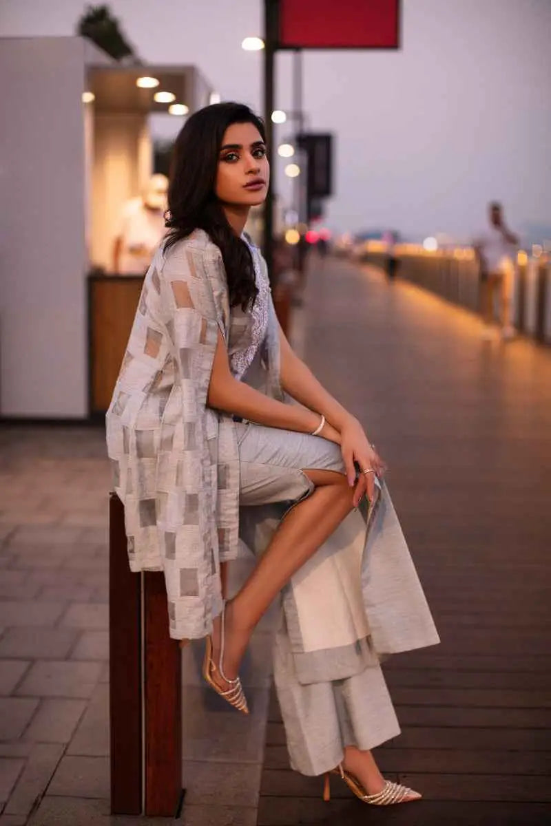 A woman wearing the silver illusion open-front geometric cape over matching trousers with gold heels