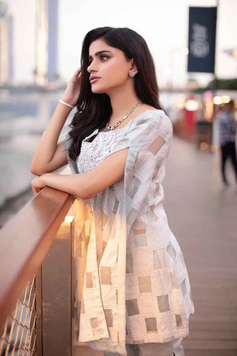 A woman wears a light gray silver illusion cape with intricate silver embroidery and geometric patterned panels