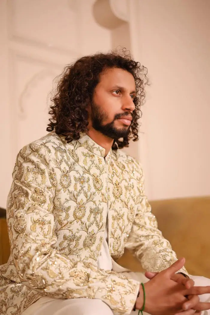 A man wearing a cream-colored sultan jacket with intricate gold embroidery and embellishments