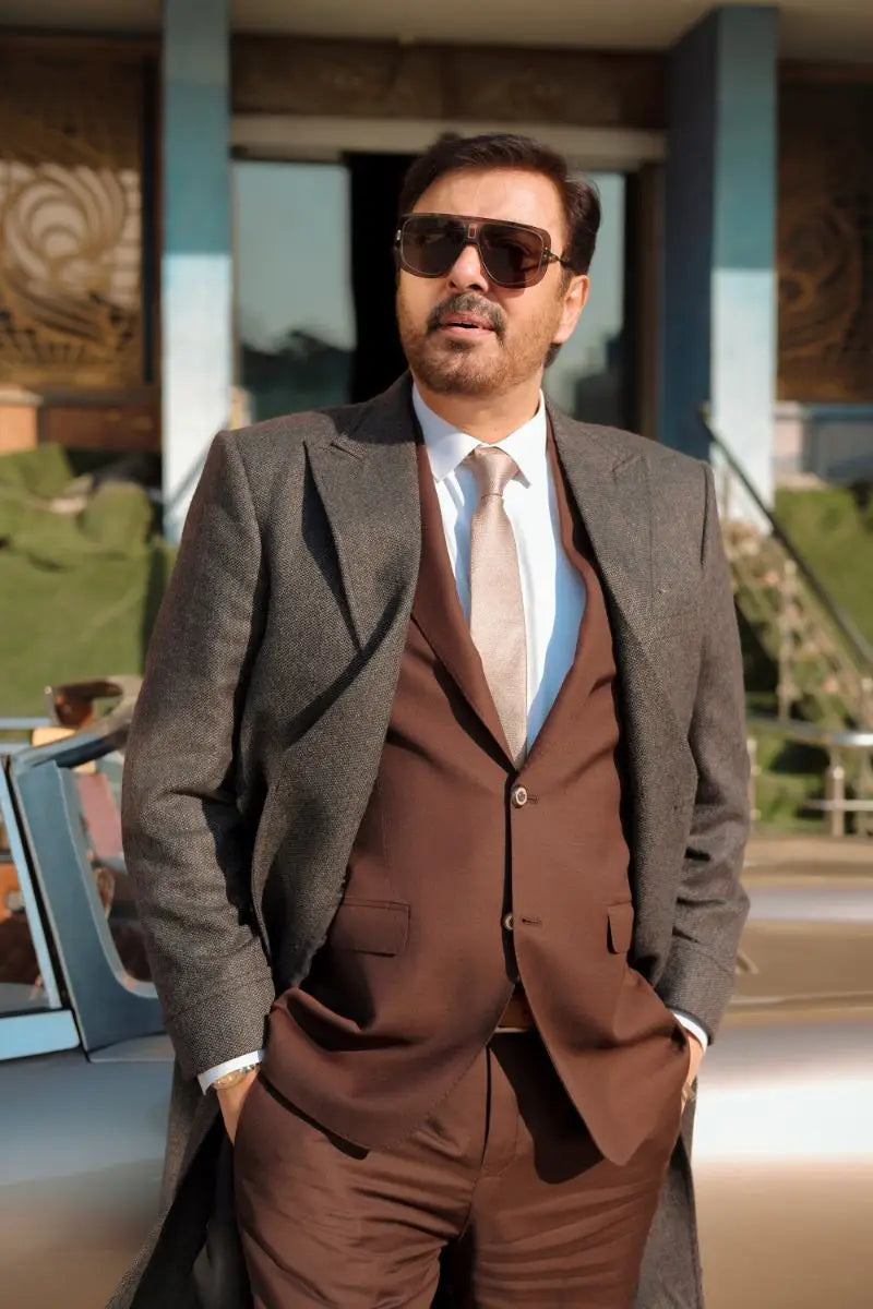 A man wearing a gray textured overcoat and brown three-piece suit with light pink tie in waheed murad virsa-e-sitaaran edit26