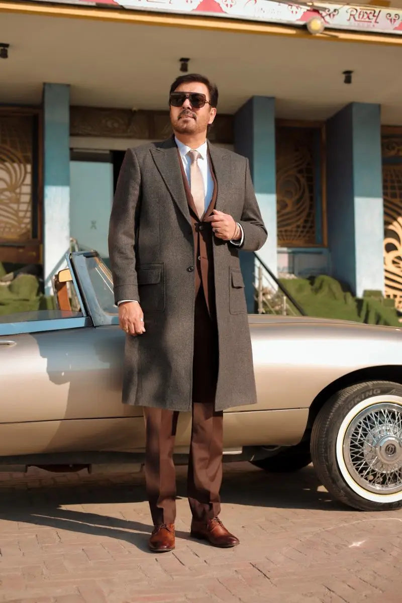 A man in a tailored gray overcoat with brown trousers stands beside a vintage silver convertible in waheed murad virsa-e-sitaaran edit 26