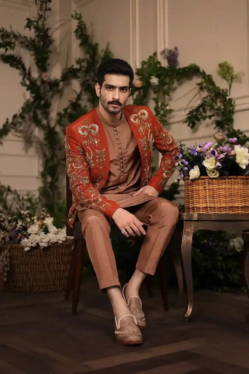 The wazir khan jacket features rich red embroidery with gold floral patterns paired with brown trousers and tan loafers