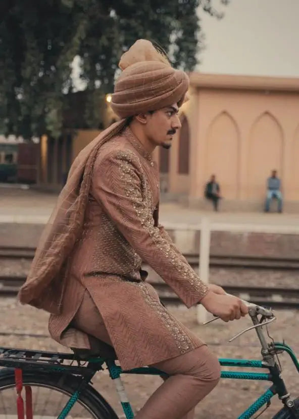 A man wearing a brown embroidered kurta and matching turban rides a vintage teal bicycle by zarposh